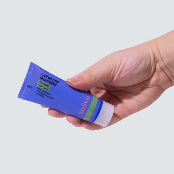 Pessoa segurando o Hidratante Reparador Sallve em bisnaga azul, ideal para aplicar no rosto e corpo com pele sensível.