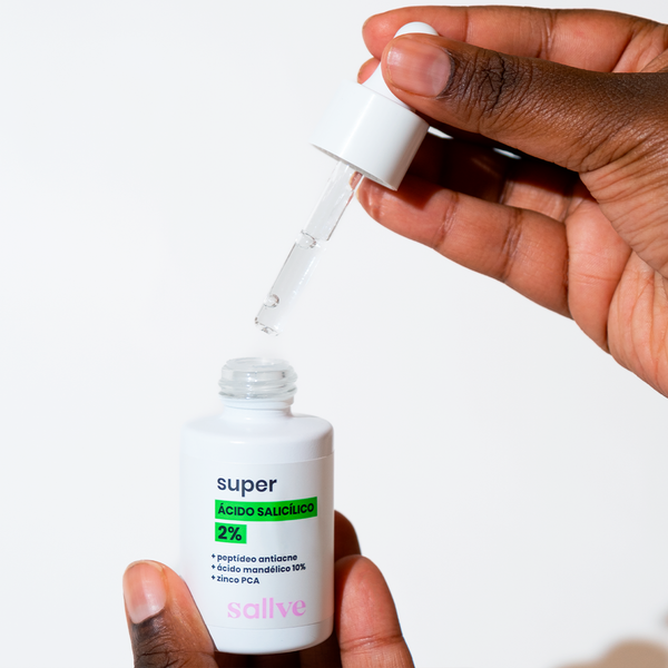 Pessoa segurando o frasco do Super Ácido Salicílico 2% da Sallve enquanto aplica uma gota do produto com conta-gotas. Sérum facial com ácido mandélico 10%, peptídeo antiacne e zinco PCA.